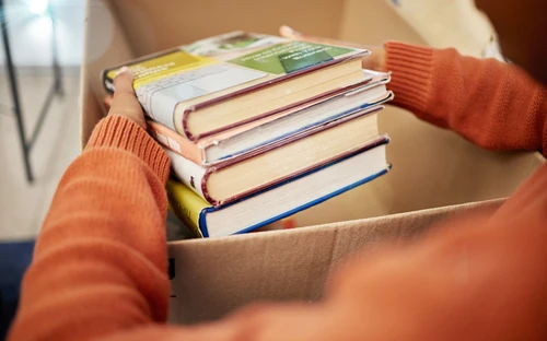 Person in orange sweater packing books into a box